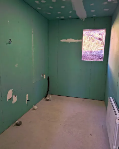 Cuarto húmedo cerrado con placa hidrófuga verde y tomas de agua vistas